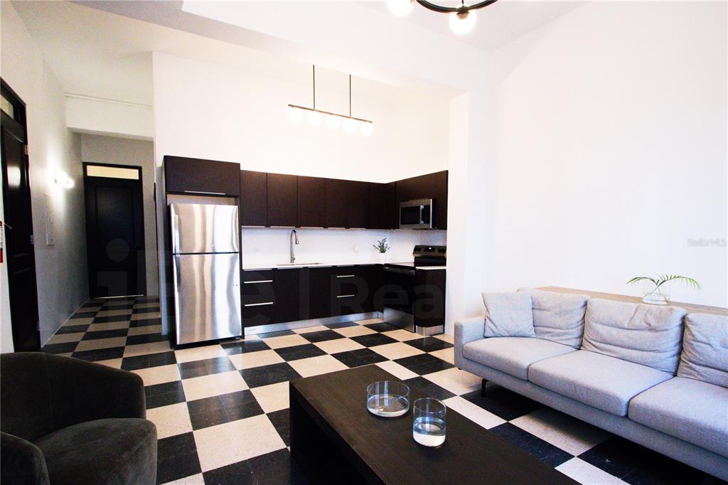 A living room with a checkered floor, a grey sofa, and an open kitchen area — 254-256 SAN FRANCISCO STREET UNIT 201, SAN JUAN, PR