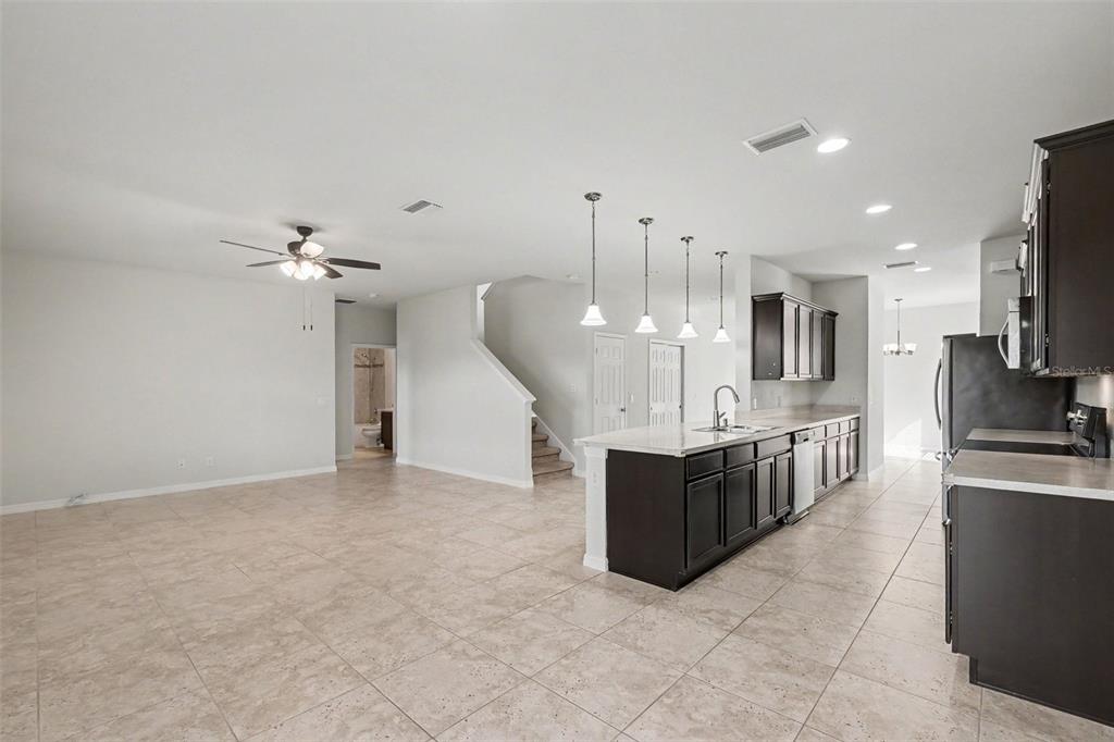 An open-concept kitchen and living area features dark wood cabinets, a kitchen island, and tile flooring — 9217 EUROPEAN OLIVE WAY, RIVERVIEW, FL