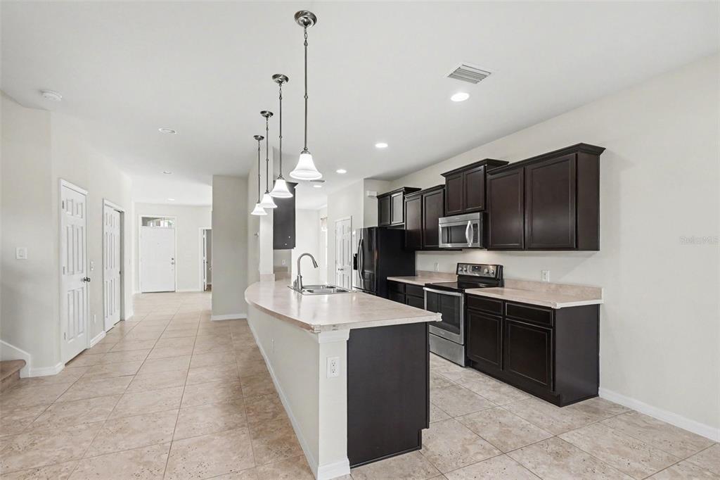 A kitchen features dark wood cabinets, stainless steel appliances, and a curved island with pendants — 9217 EUROPEAN OLIVE WAY, RIVERVIEW, FL