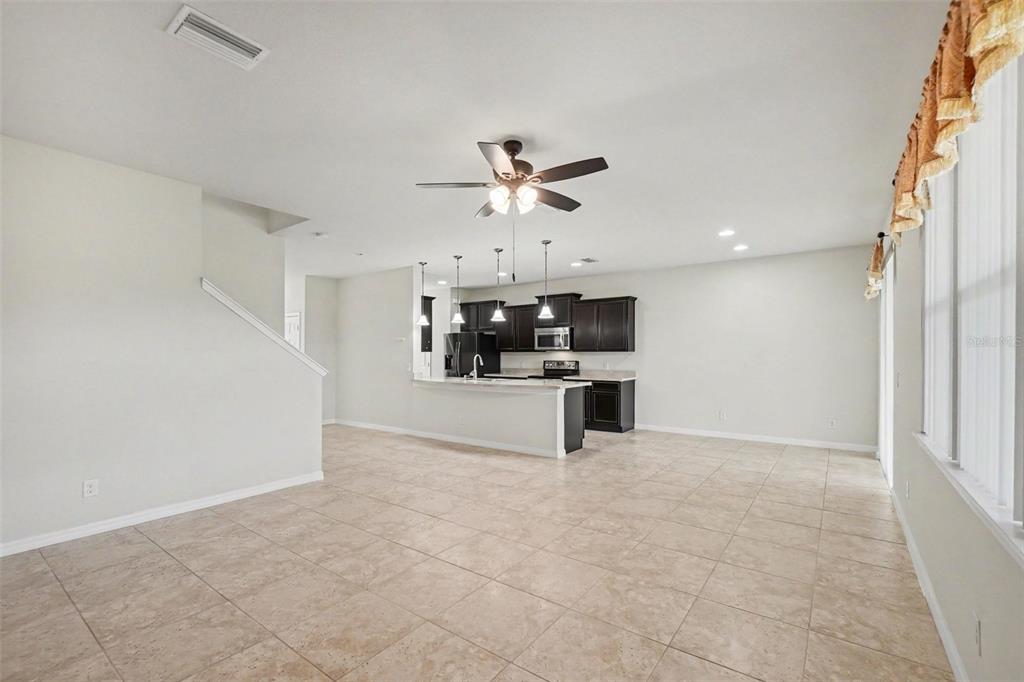 An open-concept kitchen with dark cabinets and a breakfast bar overlooks a tiled living area — 9217 EUROPEAN OLIVE WAY, RIVERVIEW, FL