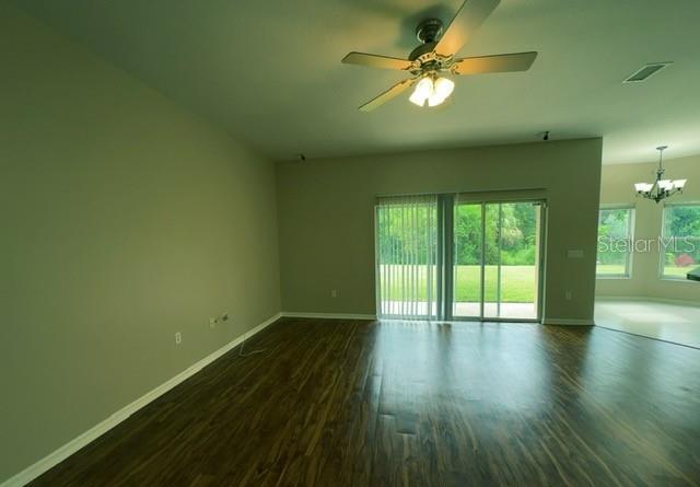 An empty living room features dark wood-look flooring, a ceiling fan, and sliding glass doors — 3161 WINDING TRAIL, KISSIMMEE, FL
