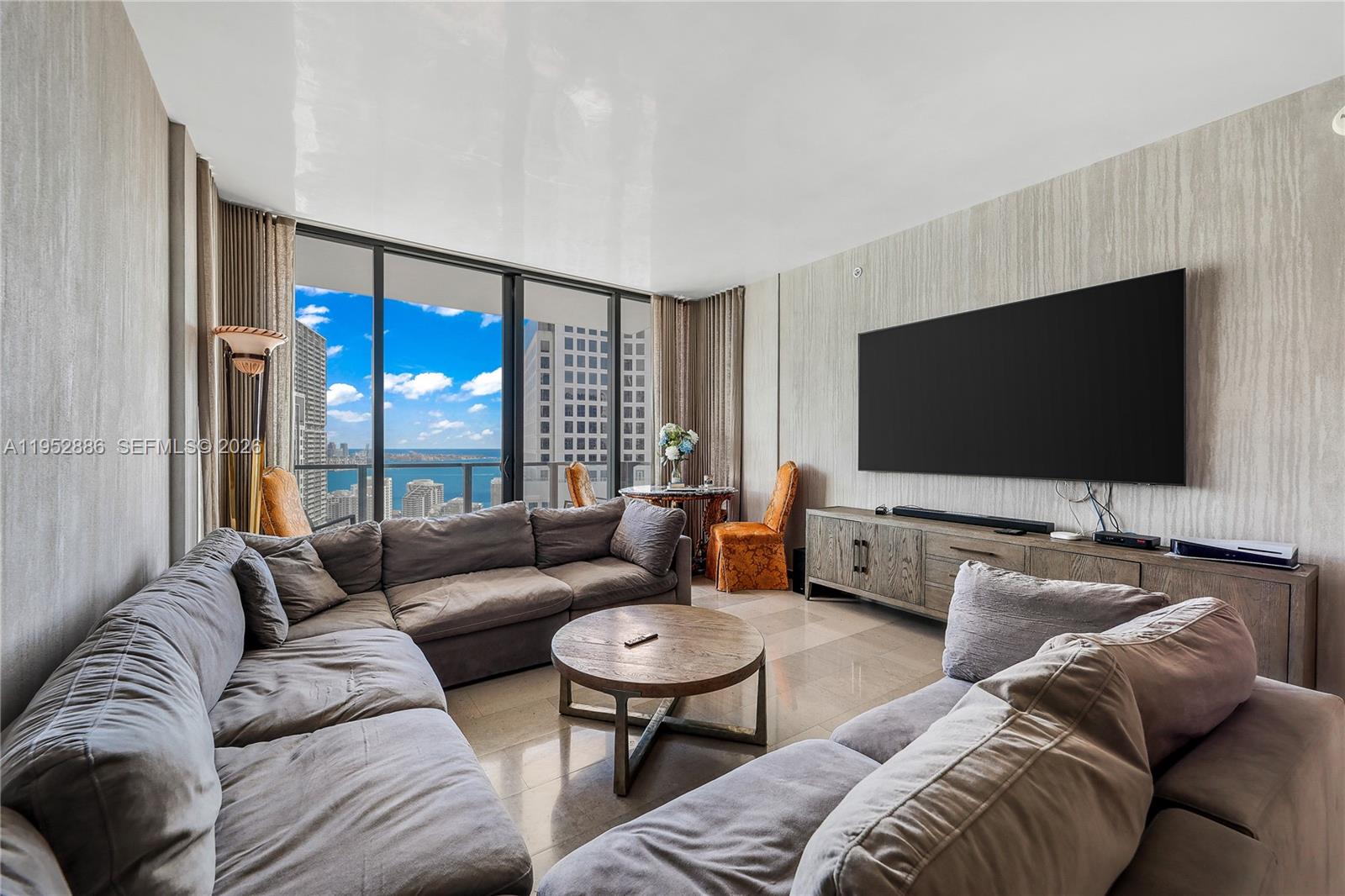 A living room features a large sectional sofa, a round coffee table, and floor-to-ceiling windows — 68 SE 6th St # 3309, Miami FL 33131, MIAMI, FL