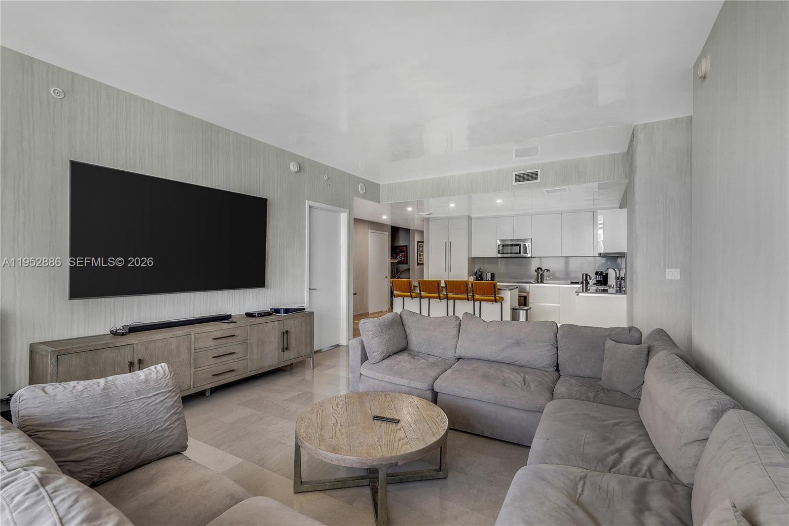 A living room with a large gray sectional sofa, a television, and an open kitchen — 68 SE 6th St # 3309, Miami FL 33131, MIAMI, FL