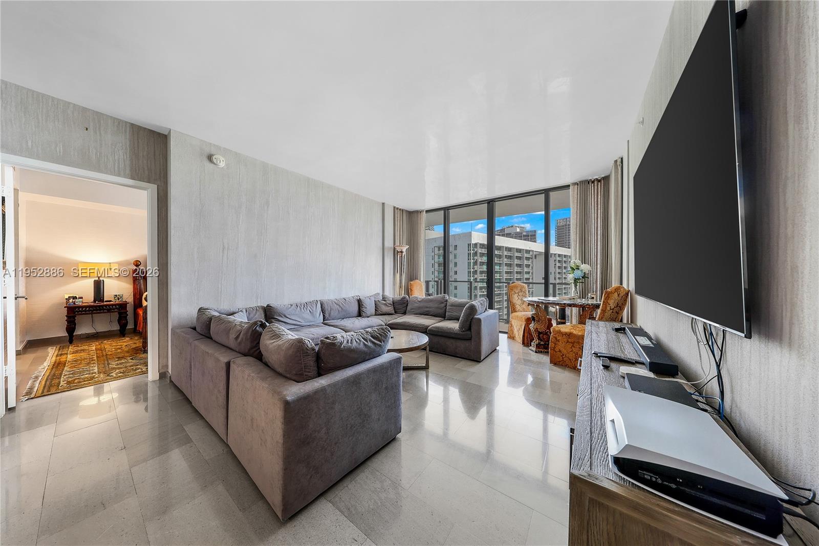 A living room features a large gray sectional sofa, tile flooring, and a wall-mounted television — 68 SE 6th St # 3309, Miami FL 33131, MIAMI, FL
