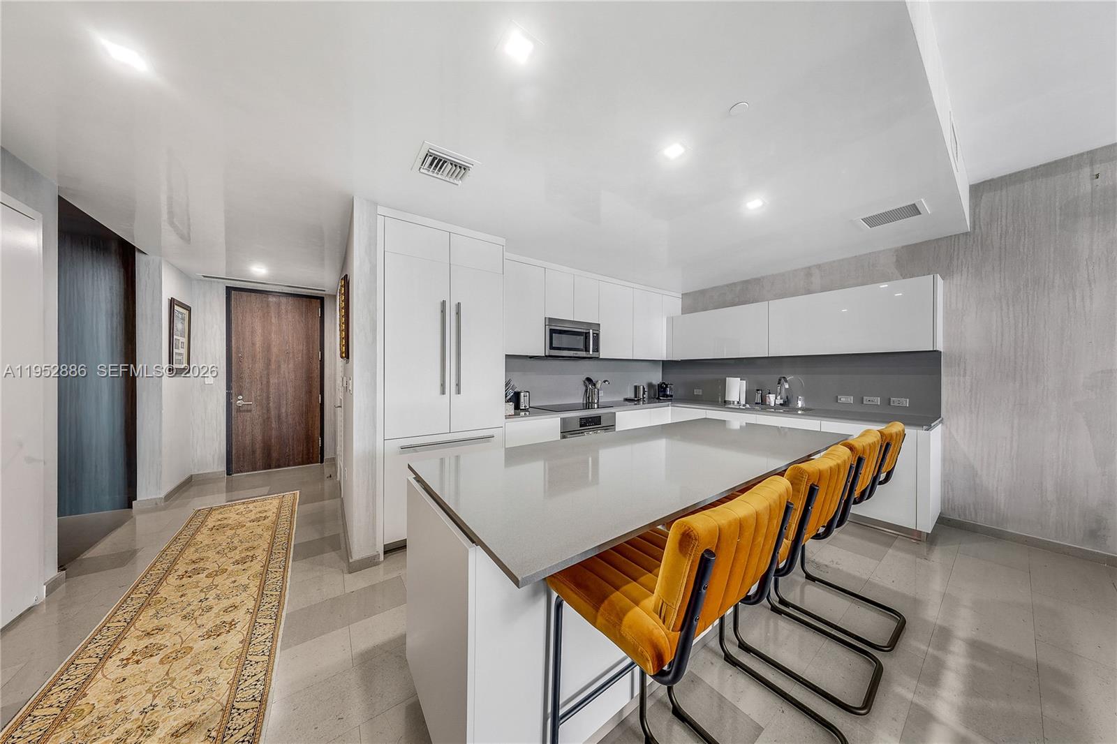A modern kitchen features white cabinetry, a gray island with orange stools, and tile flooring — 68 SE 6th St # 3309, Miami FL 33131, MIAMI, FL