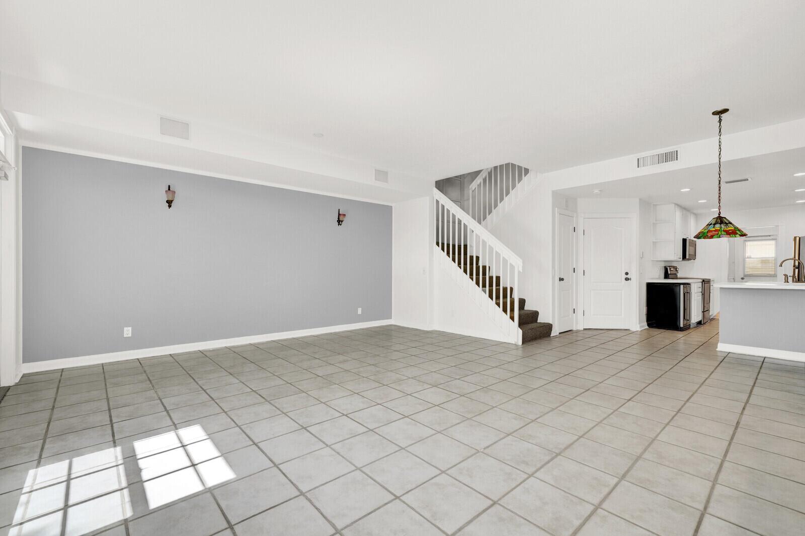 A spacious living area with gray tile flooring, a light gray accent wall, and a staircase — 133 Wentworth Court, Jupiter FL 33458, JUPITER, FL