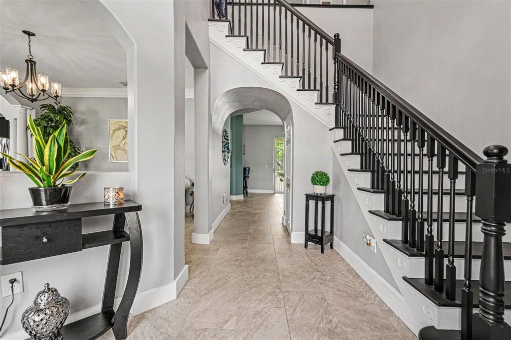 A foyer features a black staircase, tile flooring, and an arched entryway to another room — 12915 CARLINGTON LN, RIVERVIEW, FL