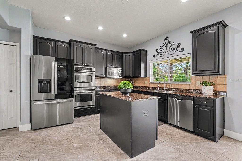 A kitchen with dark cabinets, stainless steel appliances, a center island, and granite countertops — 12915 CARLINGTON LN, RIVERVIEW, FL