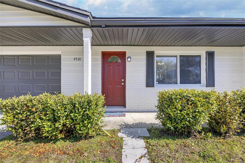A front exterior view of a house with a red door and white brick siding — 4531 AEGEAN AVENUE, HOLIDAY, FL