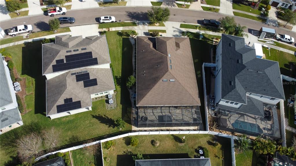 An aerial view shows three suburban houses with roofs, solar panels, and screened-in pool enclosures — 33423 AZALEA RIDGE DRIVE, WESLEY CHAPEL, FL