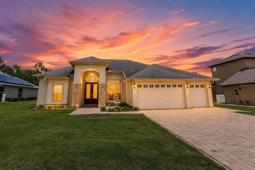 A single-story house with a stone-accented entryway, three-car garage, and a paved driveway at sunset — 4072 MISTY VIEW DRIVE, SPRING HILL, FL