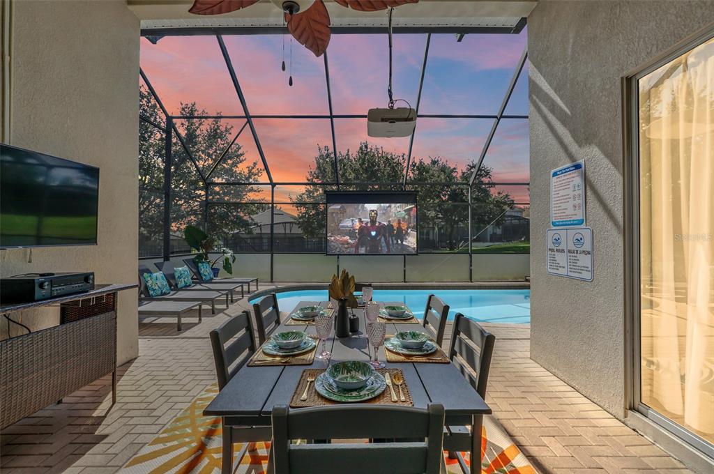 A covered patio features a dining set, a projector screen, and a swimming pool — 2630 DINVILLE STREET, KISSIMMEE, FL