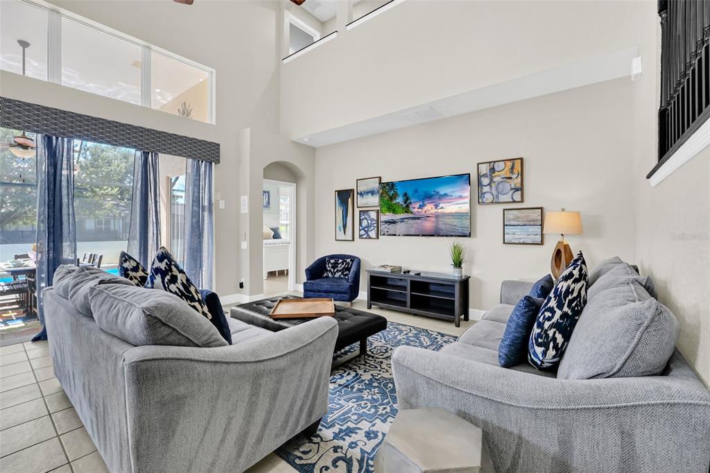 A high-ceilinged living room features gray sofas, a blue patterned rug, and a wall-mounted television — 2630 DINVILLE STREET, KISSIMMEE, FL