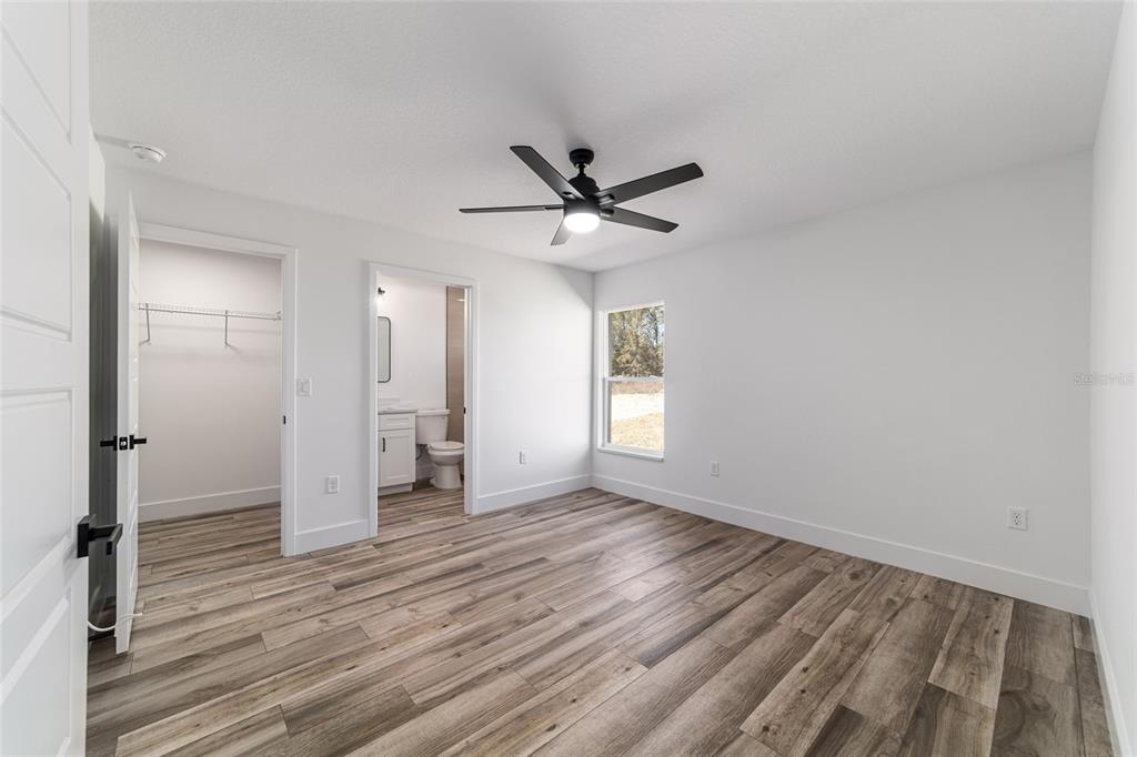 A bedroom with wood-look flooring, a ceiling fan, a walk-in closet, and an attached bathroom — 14767 SW 22 PLACE, OCALA, FL