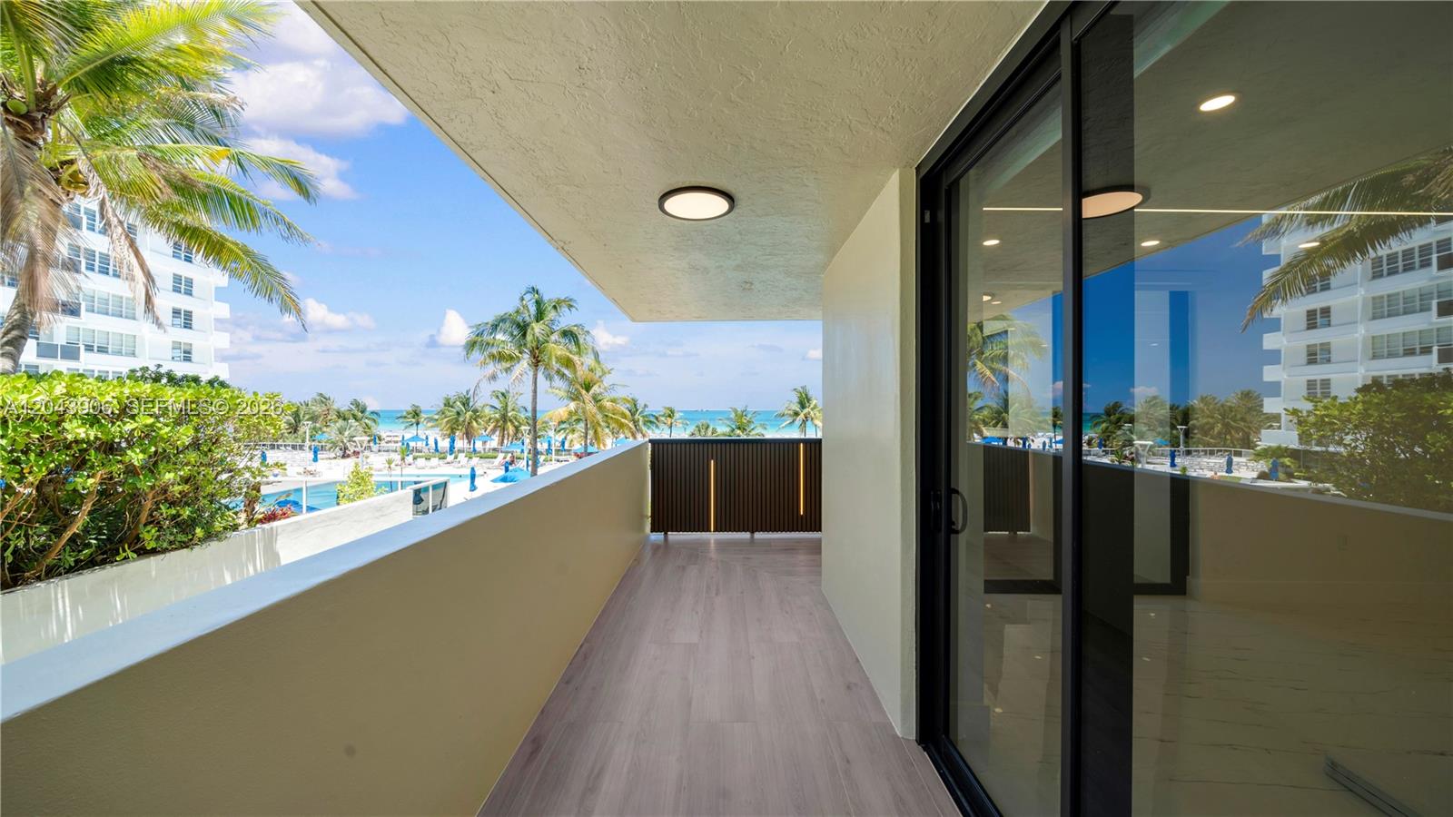 A balcony with wood-look flooring overlooks a swimming pool and the ocean — 1623 Collins Ave # 415, Miami Beach FL 33139, MIAMI BEACH, FL