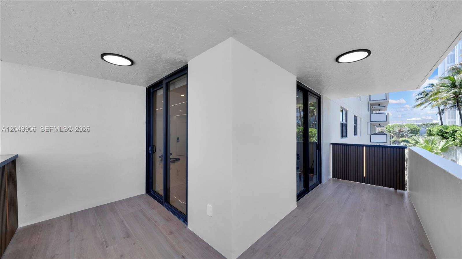 A covered balcony features light wood-look flooring, white walls, and dark-framed sliding glass doors — 1623 Collins Ave # 415, Miami Beach FL 33139, MIAMI BEACH, FL