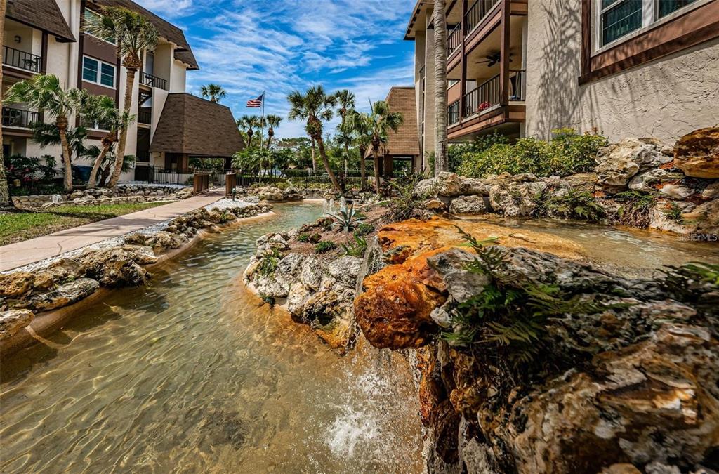 A landscaped water feature with a small waterfall flows between apartment buildings and palm trees — 3021 COUNTRYSIDE BOULEVARD UNIT 44A, CLEARWATER, FL
