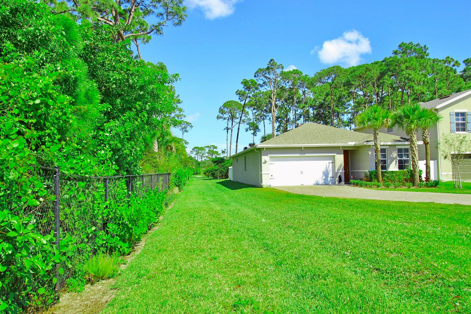 A side view of a suburban house with a garage, lawn, and chain-link fence — 2549 Timber Forest Drive, West Palm Beach FL 33415, WEST PALM BEACH, FL