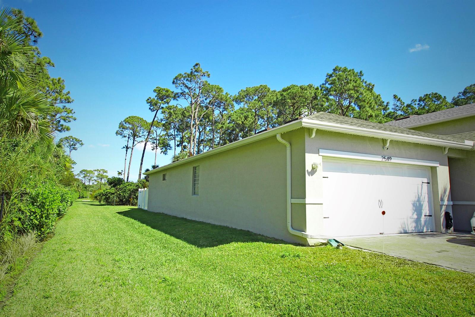 A side view of a house exterior featuring a white garage door and green lawn — 2549 Timber Forest Drive, West Palm Beach FL 33415, WEST PALM BEACH, FL