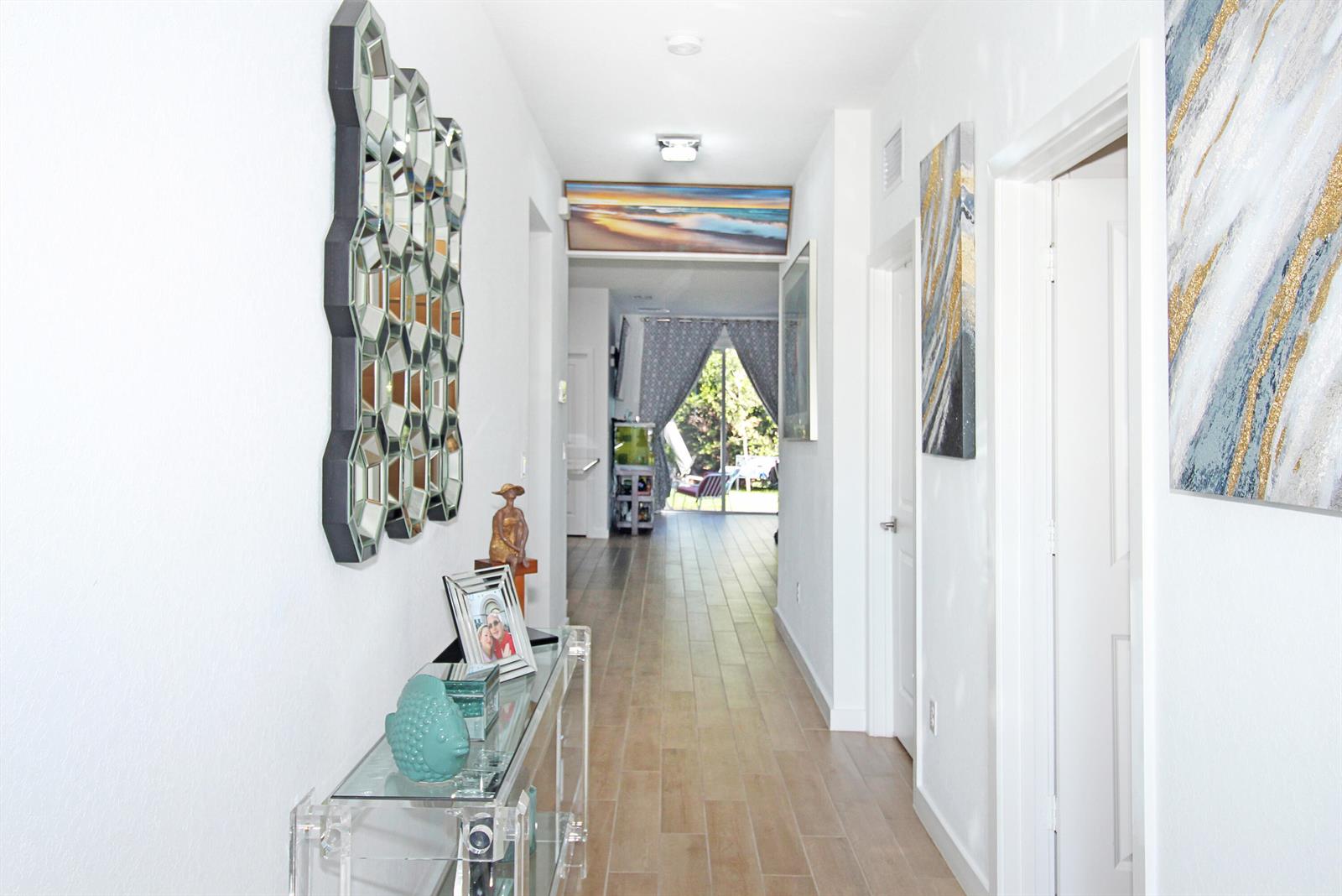 A bright hallway features a glass console table, a geometric mirror, and wood-look tile flooring — 2549 Timber Forest Drive, West Palm Beach FL 33415, WEST PALM BEACH, FL