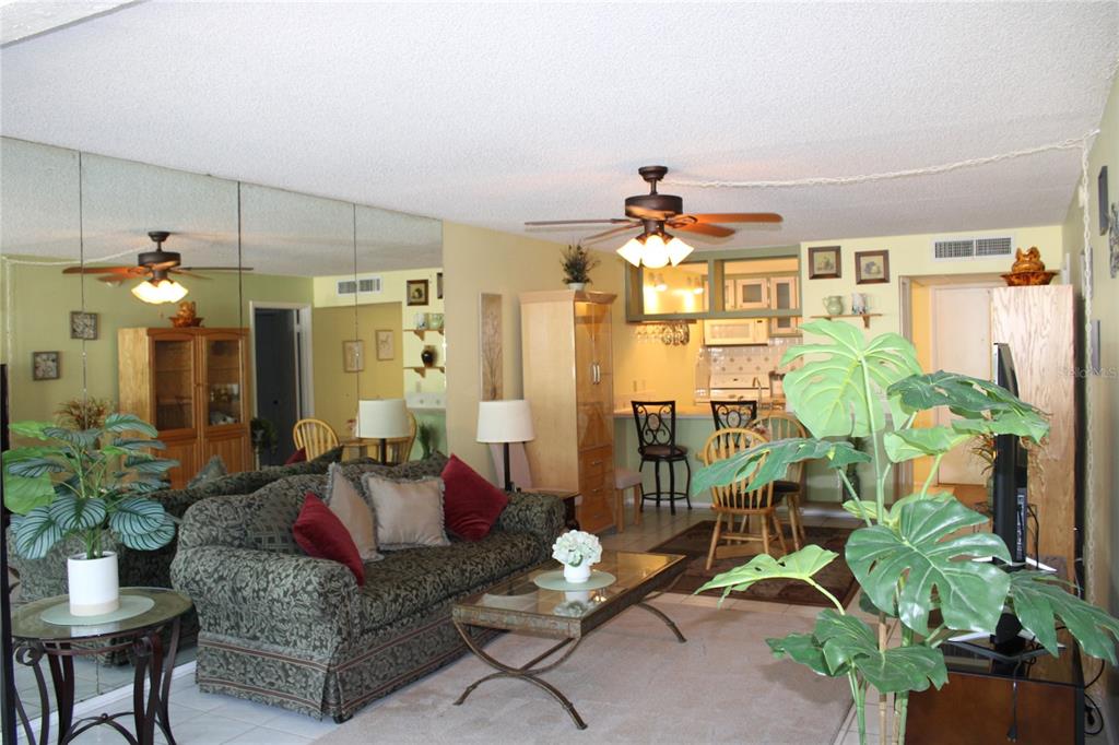 A living room with a patterned sofa, glass coffee table, mirrored wall, and adjacent dining area — 14130 ROSEMARY LANE UNIT 1117, LARGO, FL