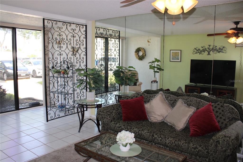 A living room features a patterned sofa, a mirrored wall, and an ornate metal screen — 14130 ROSEMARY LANE UNIT 1117, LARGO, FL