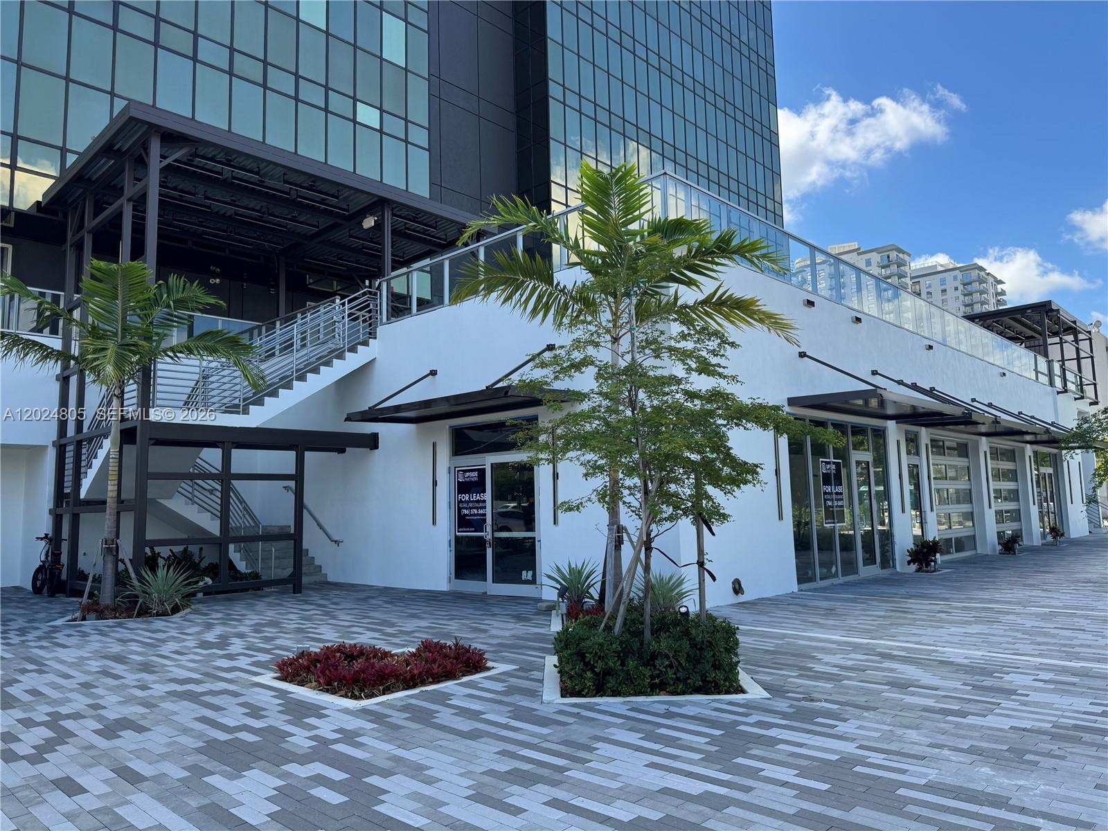 A modern commercial building exterior features a paved plaza, palm trees, and glass storefronts — 1909 Tyler St, Hollywood FL 33020, HOLLYWOOD, FL