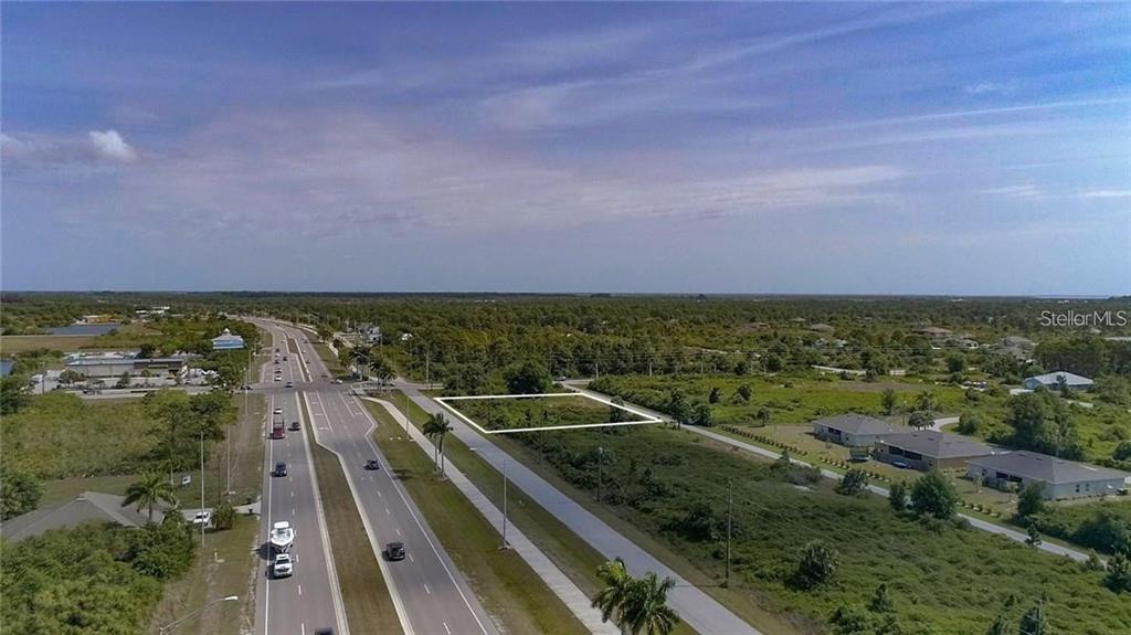 An aerial view shows a vacant rectangular lot outlined in white next to a highway — 8420 WILTSHIRE DRIVE, PORT CHARLOTTE, FL