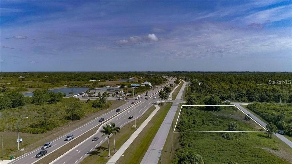 An aerial view shows a vacant, rectangular lot outlined in white next to a highway — 8420 WILTSHIRE DRIVE, PORT CHARLOTTE, FL