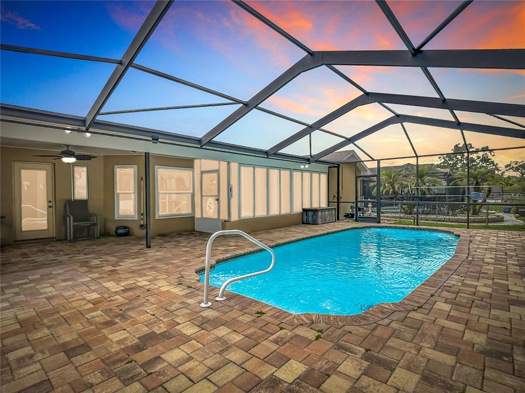 A screened-in patio features a rectangular swimming pool with a metal handrail and paver decking — 18817 PARADE ROAD, HUDSON, FL
