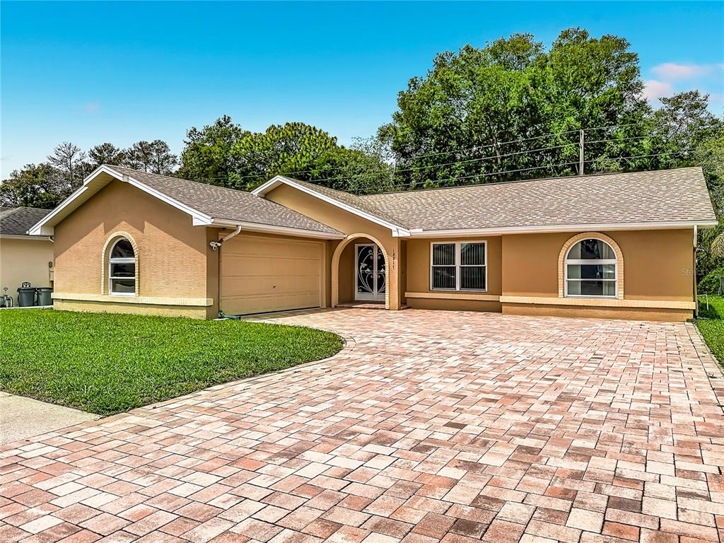 A single-story house with a tan stucco exterior, arched windows, and a paved driveway — 18817 PARADE ROAD, HUDSON, FL