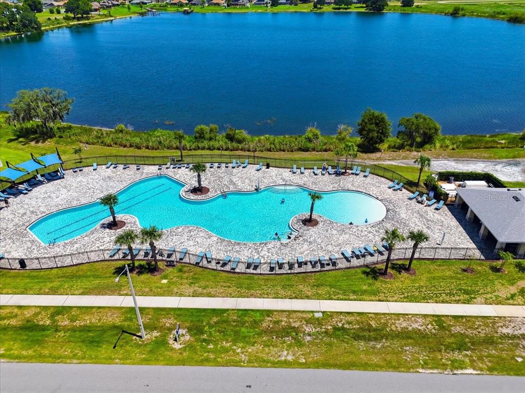 An aerial view shows a large, irregularly shaped swimming pool beside a lake — 417 CORSO LOOP, WINTER HAVEN, FL