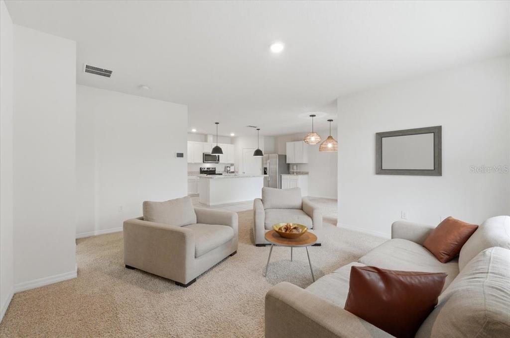 A living room with beige carpet and furniture opens to a kitchen with white cabinets — 417 CORSO LOOP, WINTER HAVEN, FL