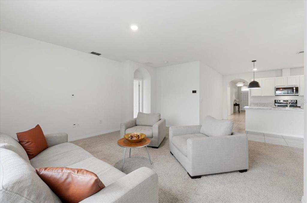 A living room with light gray carpet, neutral furniture, and an open kitchen in back — 417 CORSO LOOP, WINTER HAVEN, FL