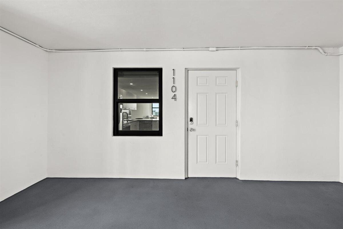 A white exterior wall features a black-framed window, a white door, and the number 1104 — 1401 N Riverside Drive # 1104, Pompano Beach FL 33062, POMPANO BEACH, FL