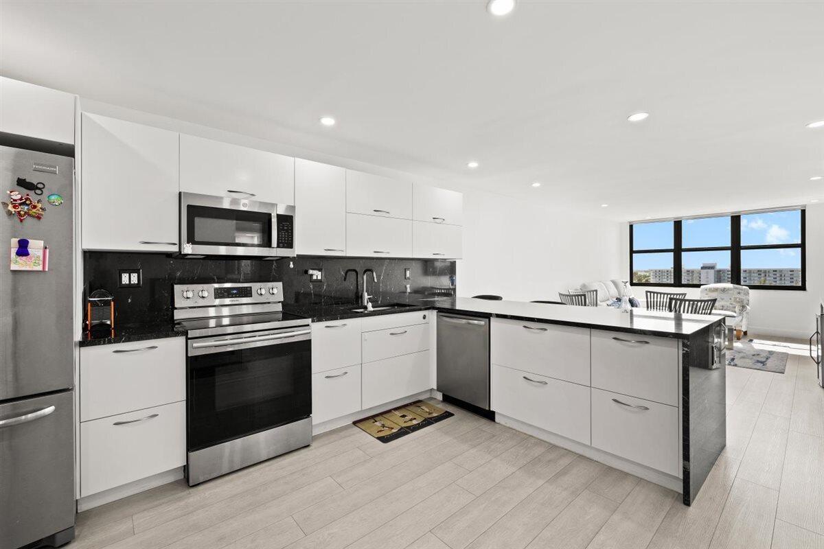 A modern kitchen features white cabinets, black countertops, stainless steel appliances, and light wood flooring — 1401 N Riverside Drive # 1104, Pompano Beach FL 33062, POMPANO BEACH, FL
