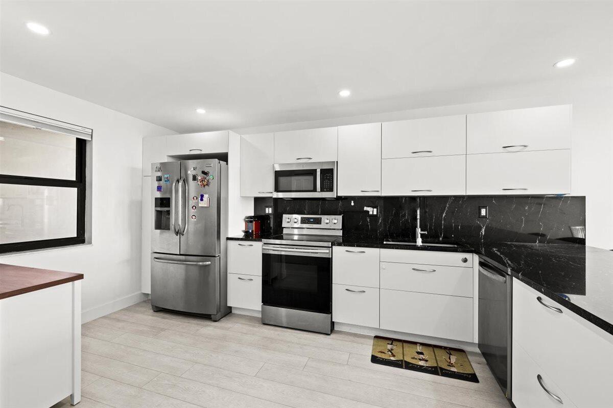 A modern kitchen features white cabinets, black marble countertops, and stainless steel appliances — 1401 N Riverside Drive # 1104, Pompano Beach FL 33062, POMPANO BEACH, FL