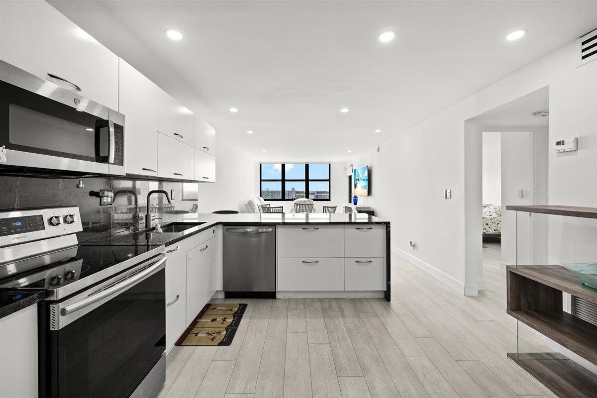 A modern white kitchen features stainless steel appliances, a peninsula, and light wood-look flooring — 1401 N Riverside Drive # 1104, Pompano Beach FL 33062, POMPANO BEACH, FL