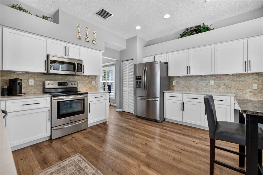 A kitchen features white cabinets, stainless steel appliances, a stone backsplash, and wood-look flooring — 11123 CLAYRIDGE DRIVE, TAMPA, FL