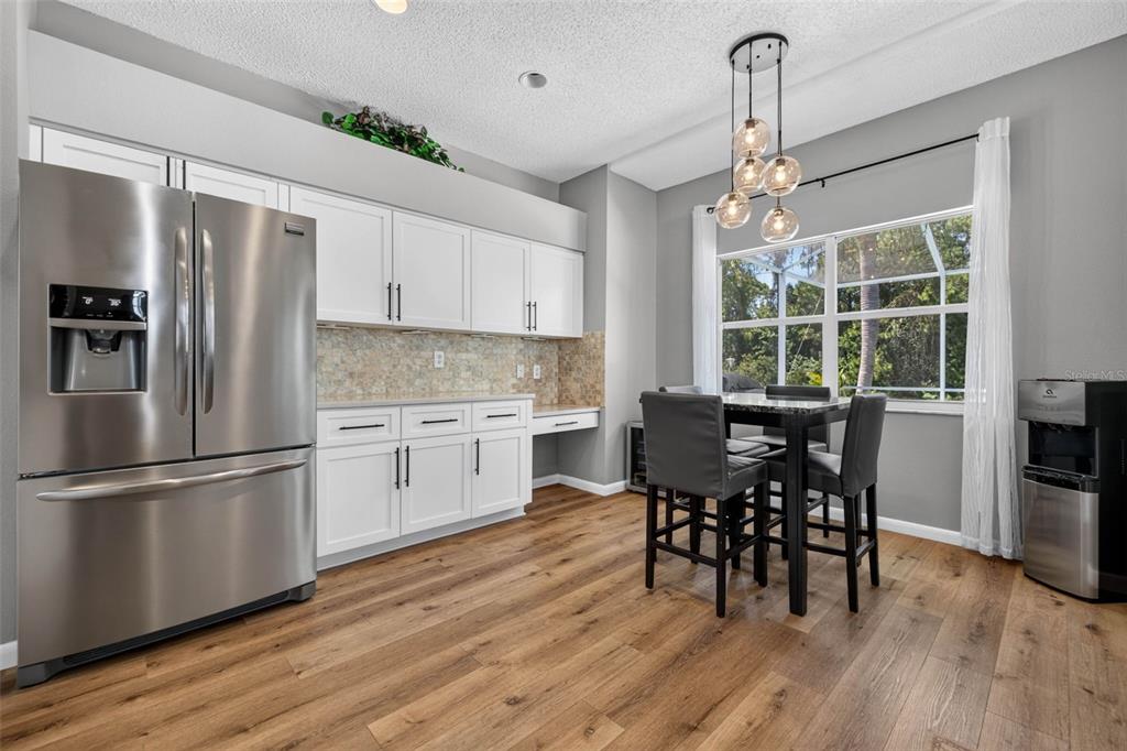 A kitchen and dining area features white cabinets, stainless steel appliances, and wood-look flooring — 11123 CLAYRIDGE DRIVE, TAMPA, FL