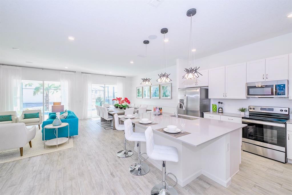 A modern open-concept kitchen and living area with white cabinetry, stainless appliances, and tile flooring — 2560 SHANTI DRIVE, KISSIMMEE, FL