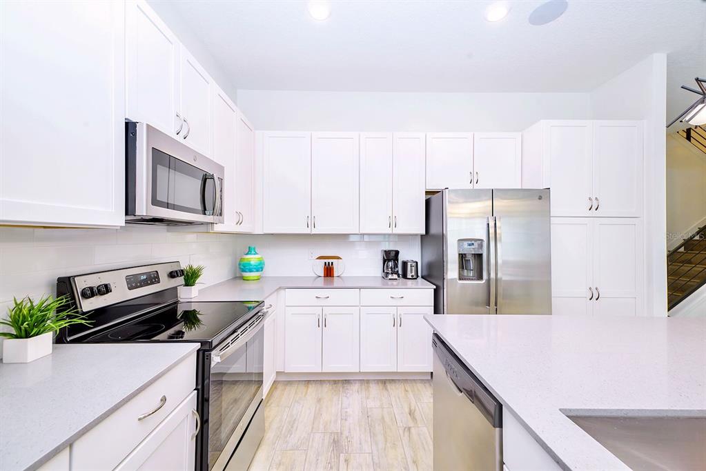 A modern kitchen features white cabinets, stainless steel appliances, and light-colored quartz countertops — 2560 SHANTI DRIVE, KISSIMMEE, FL