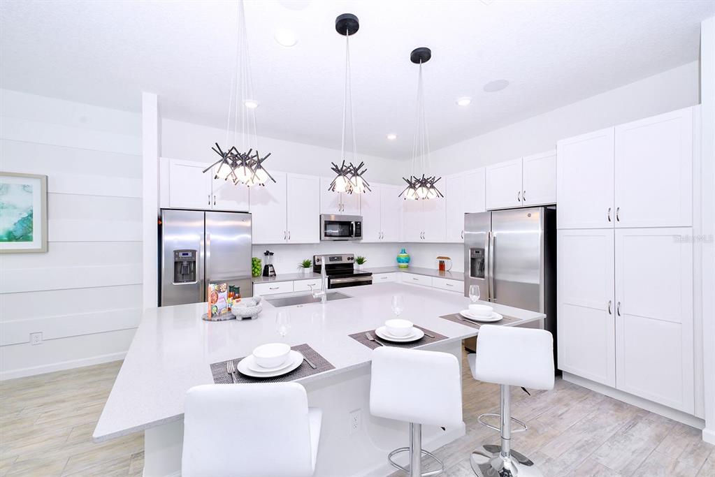 A modern white kitchen features a large island, stainless steel appliances, and pendant lighting — 2560 SHANTI DRIVE, KISSIMMEE, FL