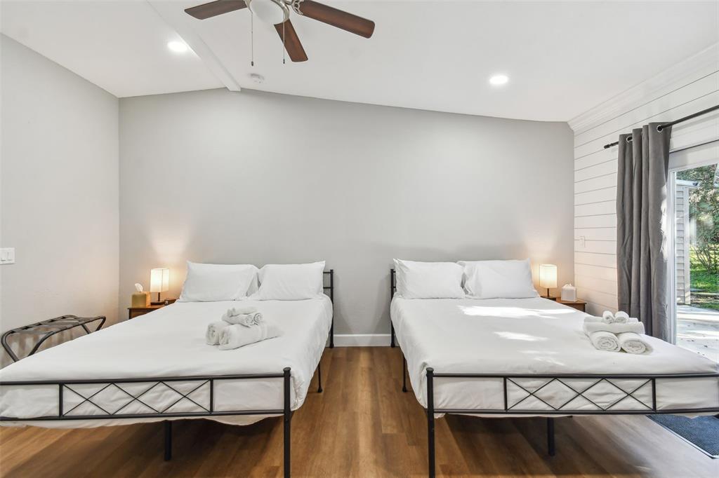 A bedroom features two beds with metal frames, wood-look flooring, and a sliding glass door — 414 JOYCE AVENUE, TEMPLE TERRACE, FL