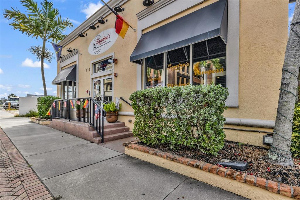 The exterior of a yellow building features a restaurant entrance, a black awning, and landscaping — 111 W OLYMPIA AVENUE, PUNTA GORDA, FL