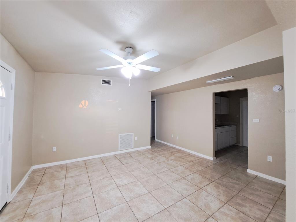 A room with beige walls, tiled floors, and a ceiling fan leads to a kitchen — 3934 CONWAY BOULEVARD, PORT CHARLOTTE, FL