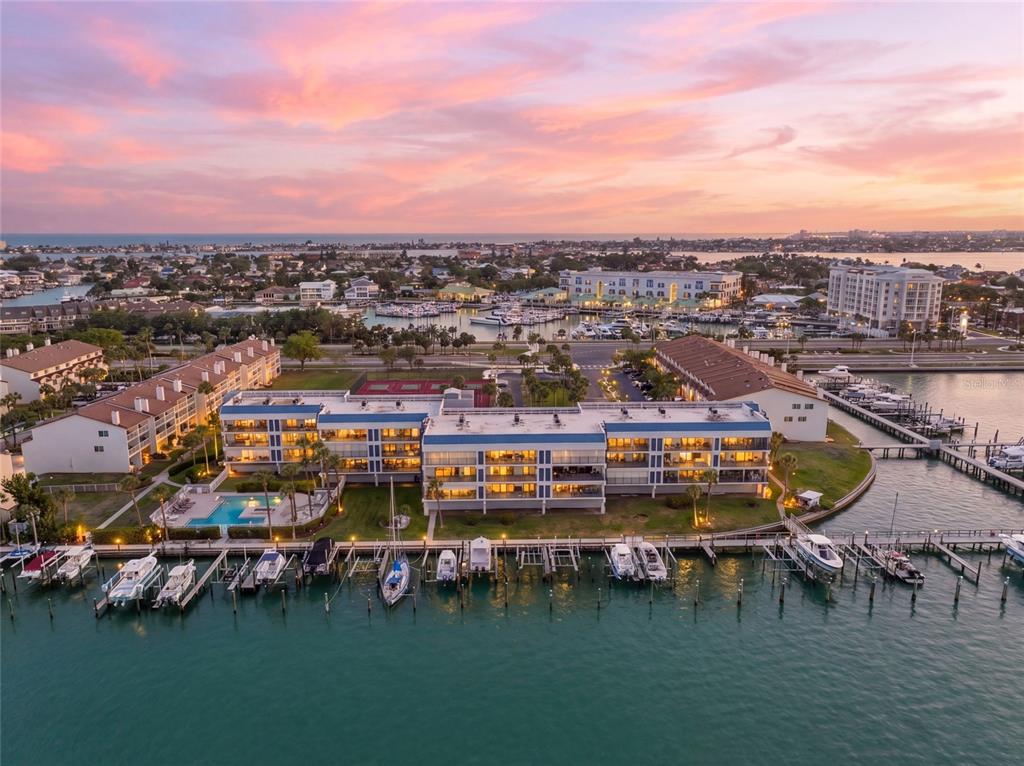 An aerial view shows a multi-story apartment building with a parking lot at sunset — 363 PINELLAS BAYWAY S UNIT 29, TIERRA VERDE, FL