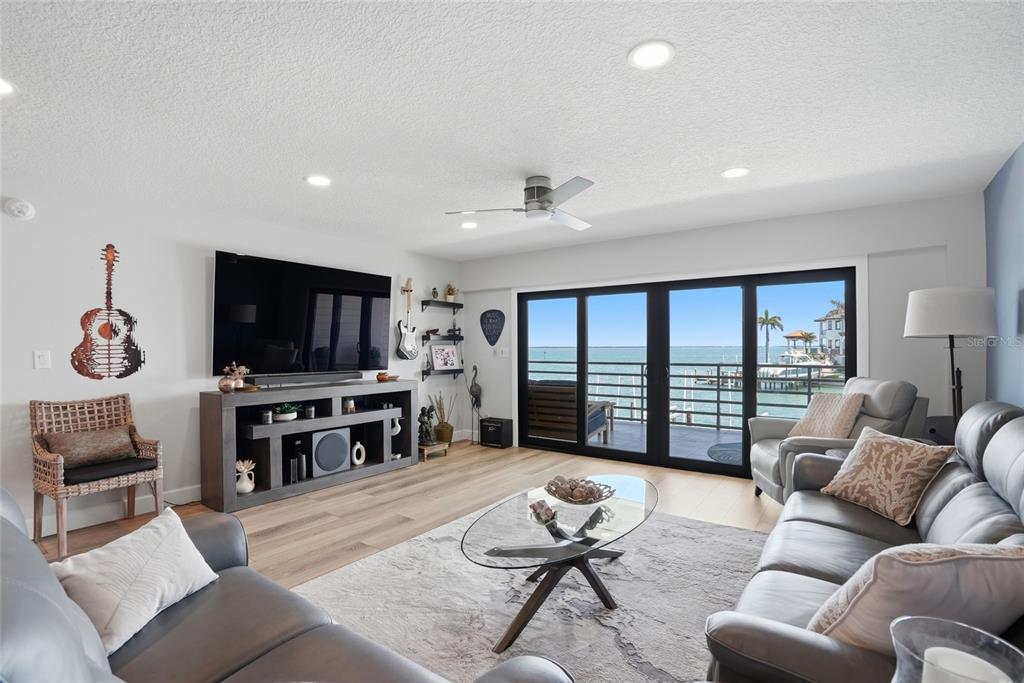 A living room features gray leather furniture, a media console, and sliding doors overlooking water — 363 PINELLAS BAYWAY S UNIT 29, TIERRA VERDE, FL