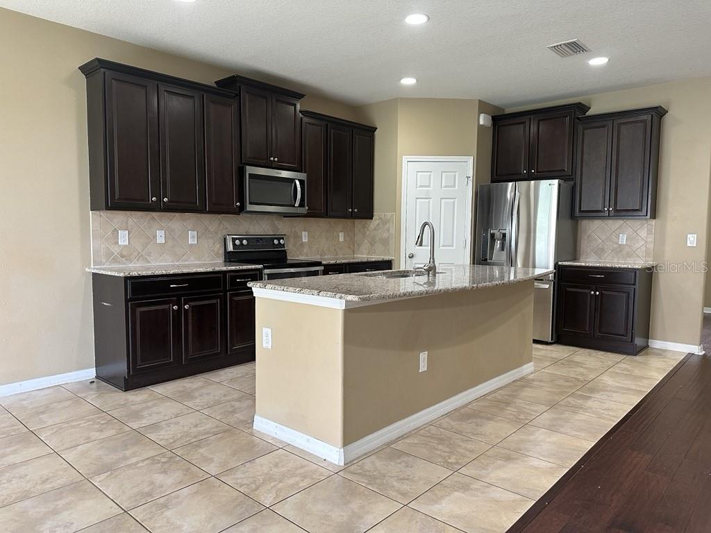 A kitchen features dark wood cabinets, granite countertops, a center island, and stainless steel appliances — 3034 WINGLEWOOD CIRCLE, LUTZ, FL