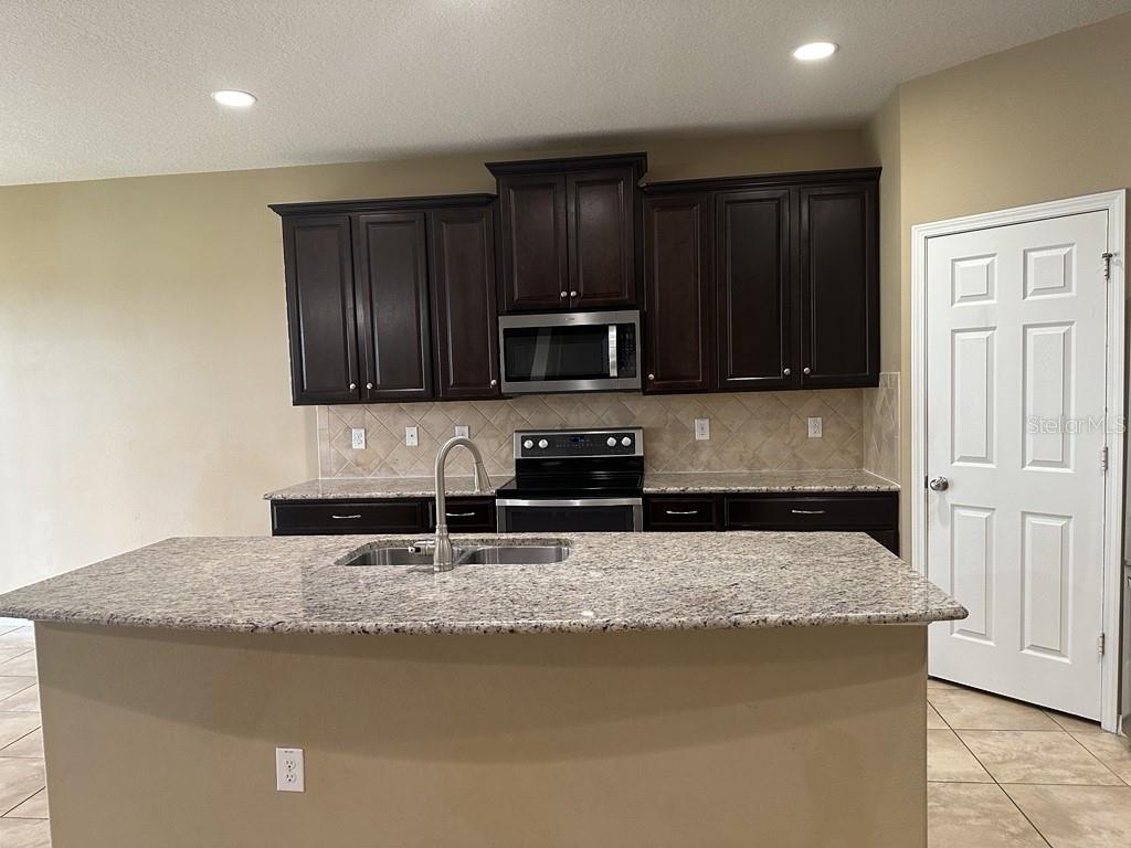 A kitchen features dark wood cabinets, granite countertops, a center island, and stainless steel appliances — 3034 WINGLEWOOD CIRCLE, LUTZ, FL